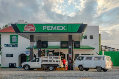 Huatulco, Oaxaca, Meksika. 14 Aralık 2025. Bulutlu bir günde yakıt dolduran bir görevli ve iki aracın yer aldığı yeşil ve beyaz gölgelikleriyle bir PEMEX benzin istasyonunun dış görünüşü.