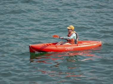 Huatulco, Oaxaca, Meksika. Aralık 18, 2025. Orta ölçekli bir atış can yeleği ve sarı şapkalı bir kadını okyanus suyunda kırmızı bir Hobie Lanai kanosuyla kayarken yakalar..