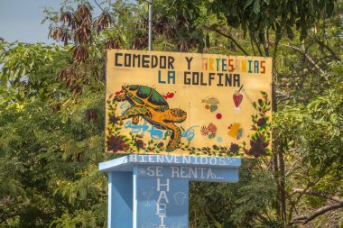 Meksika 'da yemyeşil ağaçlara karşı boyalı bir deniz kaplumbağası ve yiyecek ikonları içeren renkli yol kenarı iş tabelası. Huatulco, Oaxaca, Meksika 'da göz hizasında.