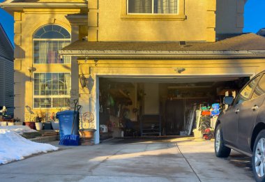 Calgary, Alberta, Kanada. 23 Aralık 2025. Geniş bir açı, sıcak kış günbatımında garaj yolu karla kaplı dağınık bir banliyö garajının göz hizasında görüntüsü..