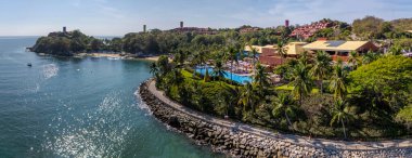 Huatulco, Oaxaca, Meksika. 26 Aralık 2025. Lüks bir sahil otelinin geniş insansız hava aracı görüntüsü. Mavi bir havuz, palmiye ağaçları ve Meksika, Huatulco 'da kayalık bir sahil şeridi. Güneşli bir gün, keskin bir odaklanma.