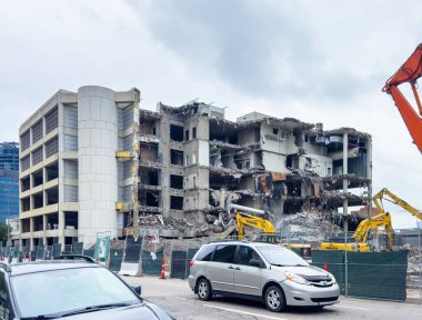 Calgary, Alberta, Kanada. Aralık 28, 2025. Kanada 'da güvenlik çitlerinin arkasında sarı Komatsu kazıcıları tarafından sökülen çok katlı beton bir yapının geniş, göz hizasında bir görüntüsü..