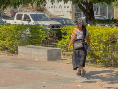 Huatulco, Oaxaca, Meksika. Aralık 28, 2025. Huatulco 'da güneşli bir meydanda yürüyen Geleneksel Meksika Giysisi içindeki Kadın