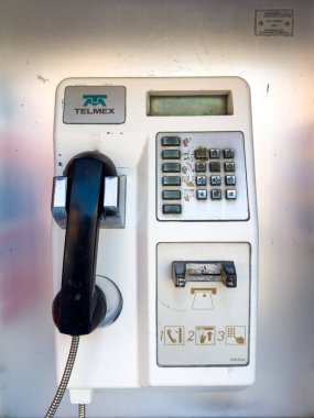 Huatulco, Oaxaca, Meksika. 27 Aralık 2025. Metalik bir duvarda telefon, tuş takımı ve kart yuvası olan yıpranmış beyaz bir Telmex ankesörlü telefonun dikey, göz hizası..