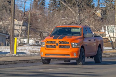 Calgary, Alberta, Kanada. 18 Ocak 2026. Kışın güneşli bir caddede siyah yarış çizgili turuncu bir Ram 1500 kamyonet..