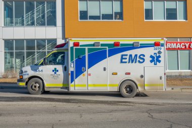 Calgary, Alberta, Kanada. 30 Ocak 2026. Alberta Sağlık Hizmetleri 'ne ait bir ambulansın yan profili modern bir binanın önündeki caddeye park edilmiş..