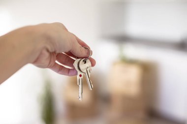 Arka planda karton kutular olan ev anahtarlarını tutan bir el kapağı. Taşınma konsepti, yeni ev, taşınma günü, yeni bir başlangıç..