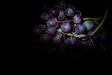 Yakın plan, siyah arka planda izole edilmiş düşük ışıkta koyu üzüm demeti..