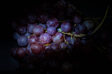 Yakın plan, siyah arka planda izole edilmiş düşük ışıkta koyu üzüm demeti..