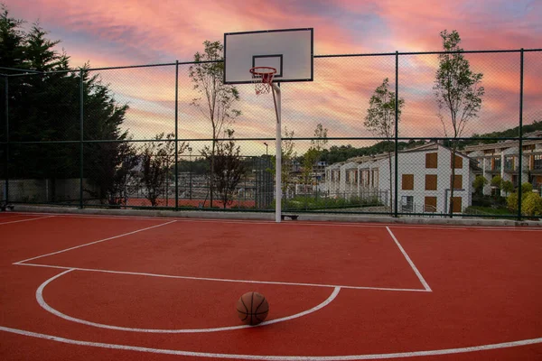 Basketball and a basket in an outdoor court with dramatic lightning.