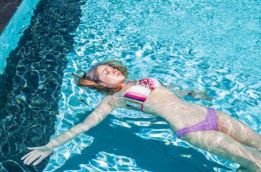 Yüzme havuzunda bikinikle yüzen güzel bir kız.