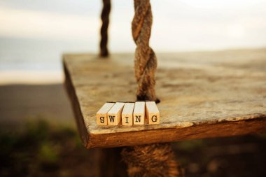 Kelime salıncağı ahşap bölmelerden yapılmış, deniz kıyısına bakan tahta bir salıncağa yerleştirilmiş. Çocukken bir çocuk parkında tatil.