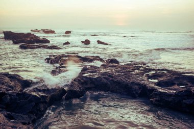 Kayalarla, parlayan güneşle ve gün batımında okyanusun dalgalarıyla güzel bir deniz manzarası..