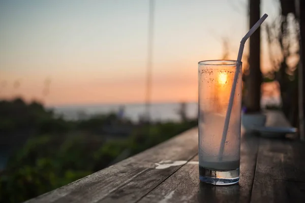 Empty glass with a straw on a wooden bar at sunset.