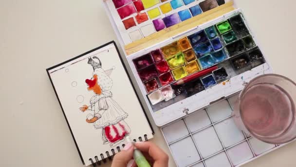 A girl painting a juggling clown with green wig using watercolors. — Vídeo de Stock