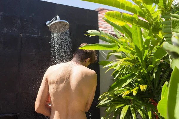 Tall strong man taking a shower. Tropical bathroom — Stock Photo, Image