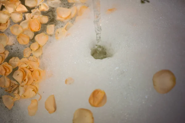 Agua que fluye en la espuma de baño con pétalos de rosa. —  Fotos de Stock