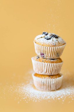 Blueberriey ve turuncu arka planlı üç muffin.