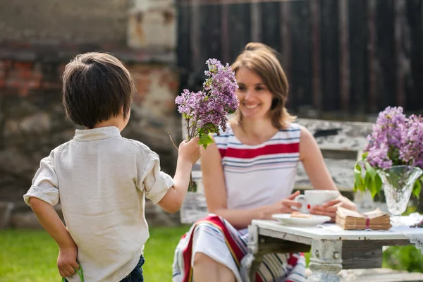 Hermosa mamá, tomando café en un patio trasero, pequeño niño lindo giv — Foto de Stock