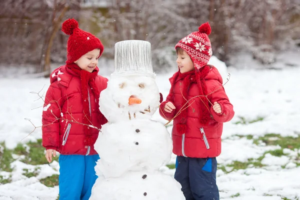 Boldog szép gyerek, testvér, épület a kertben hóember — Stock Fotó