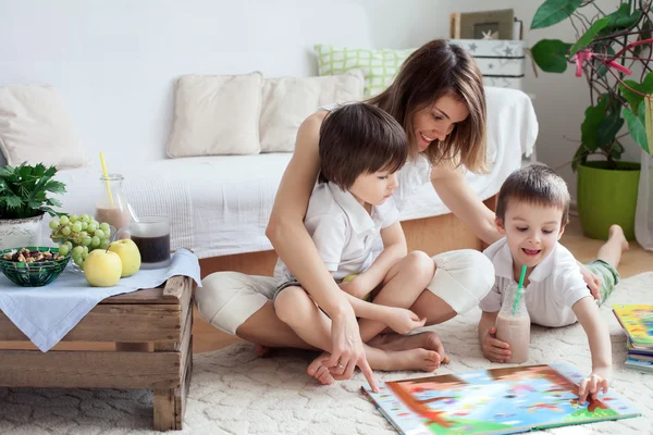 Jovem mãe, leia um livro para seus filhos, meninos, no livi — Fotografia de Stock