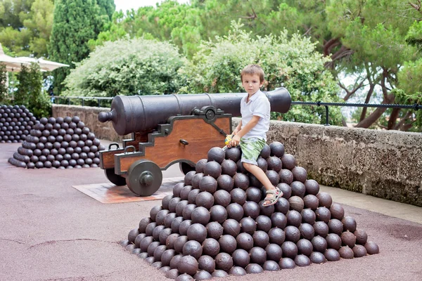 Preschool boy, sitting on a pile of cannon-balls in the village — Stock Photo, Image