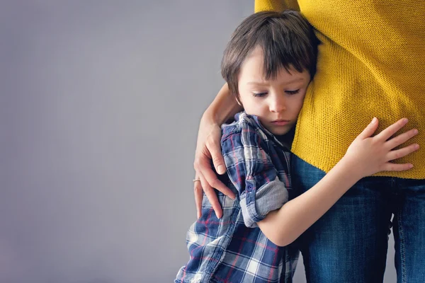 Copil trist, băiete, îmbrăţişându-şi mama acasă — Fotografie, imagine de stoc