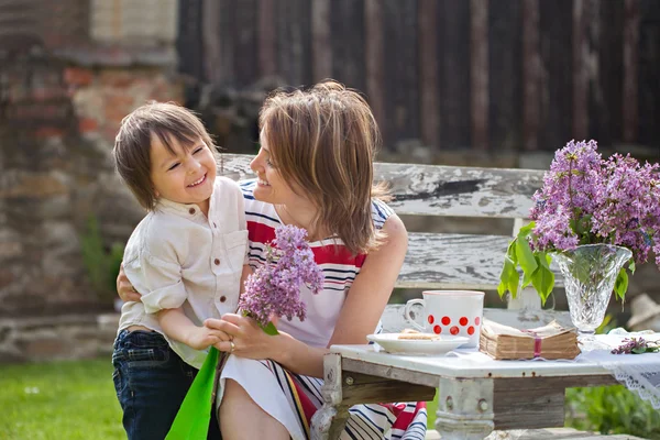 Mooie moeder, met koffie in een achtertuin, jonge schattig kind giv — Stockfoto