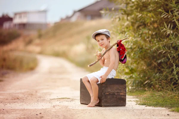 Lindo niño pequeño, sentado en una maleta grande y vieja, vintage, sosteniendo — Foto de Stock