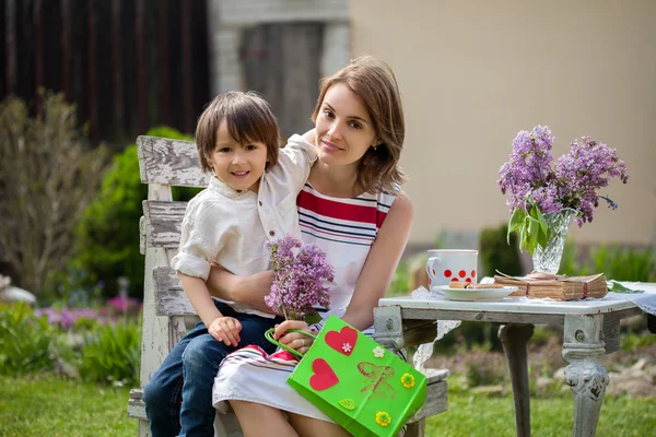 Mooie moeder, met koffie in een achtertuin, jonge schattig kind giv — Stockfoto