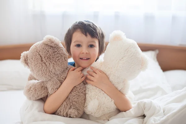 Lindo niño con osos de peluche, acostado en la cama, mirando a la cámara — Foto de Stock