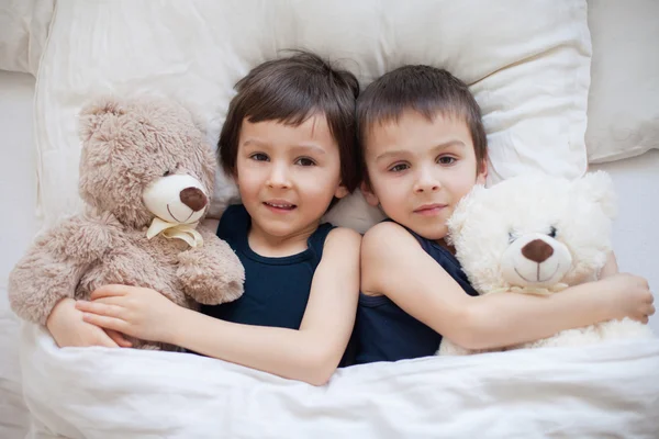 Dois meninos com ursinhos de pelúcia, deitados na cama, olhando para a câmera — Fotografia de Stock