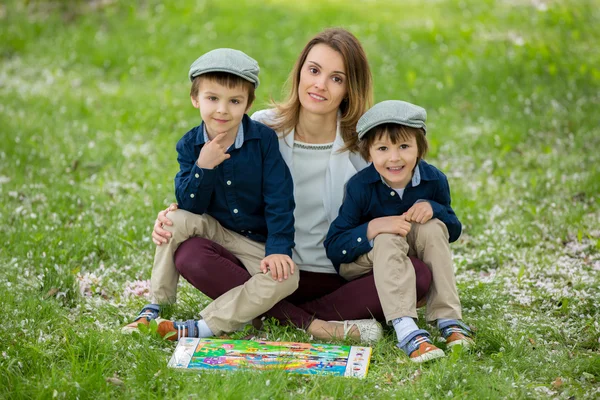 Mother with two children, boys, reading a book in a cherry bloss — Stock Photo, Image