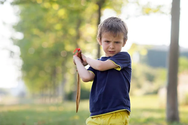 Angry little boy, holding sword, glaring with a mad face at the — Stock Photo, Image