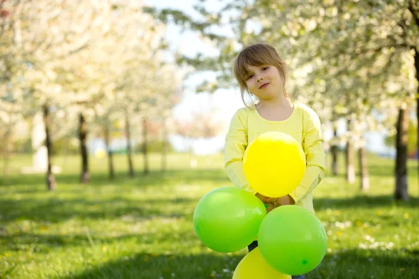 Niedliches kleines Mädchen spielt mit Luftballons in einem blühenden Apfelbaum — Stockfoto