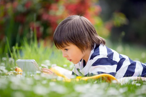 Süßer kleiner Junge, der sich im Frühlingsblumengarten hinlegt und weiter spielt — Stockfoto