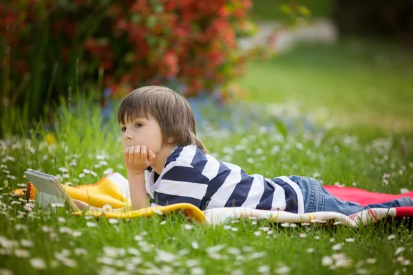 Menino doce, deitado no jardim de flores da primavera, brincando — Fotografia de Stock