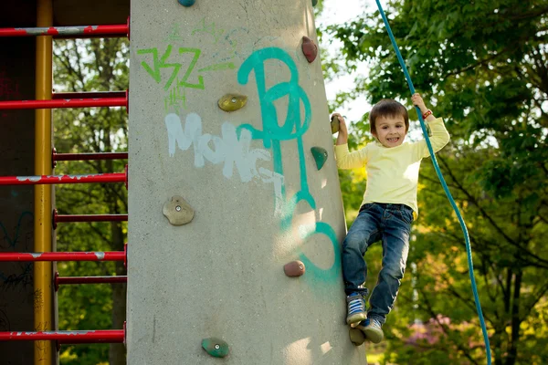 Aranyos óvodai kisfiú, mászó kötéllel rock falra — Stock Fotó