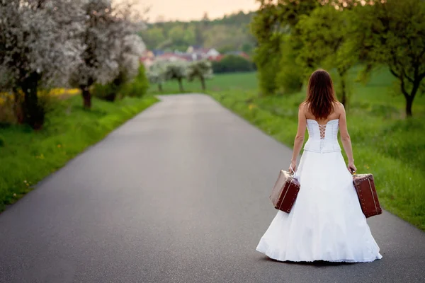 Jonge bruid op de weg met een koffer — Stockfoto