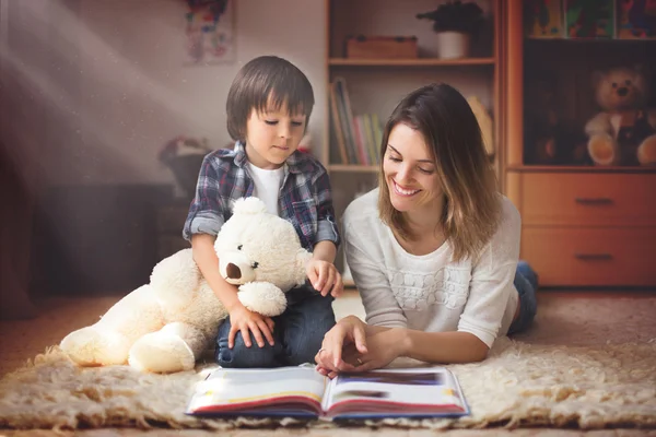 Joven madre, lee un libro a su hijo, chico en la sala de estar o — Foto de Stock