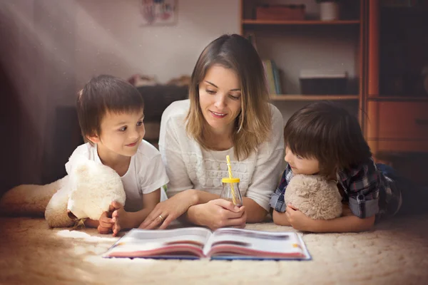 Young mother, read a book to her tho children, boys, in the livi — Stock Photo, Image