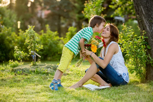 Junge schöne Mutter, im Garten sitzend, kleiner Junge, ihr Sohn — Stockfoto