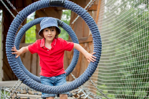 Lindo niño, niño, escalando en una estructura de patio de juegos de cuerda — Foto de Stock