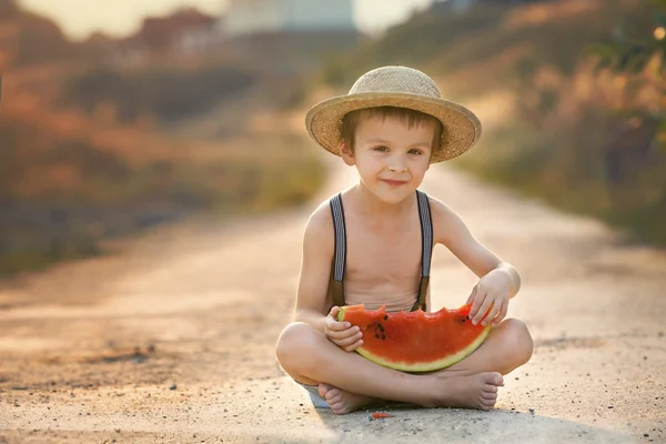 Söt liten pojke, äta vattenmelon på en lantlig by väg — Stockfoto