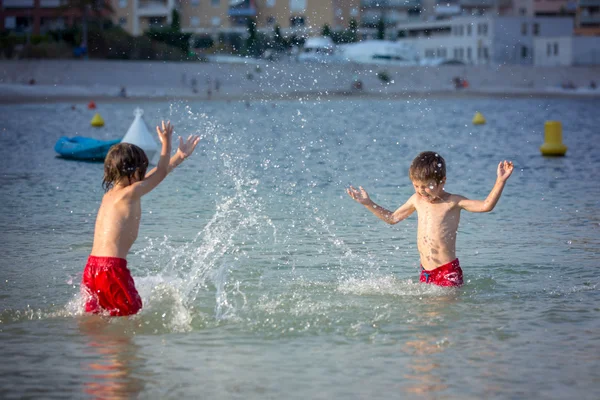 Twee lieve kinderen, spatten elkaar met water op het strand — Stockfoto
