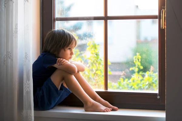 Criança triste, menino, sentado em um escudo da janela — Fotografia de Stock