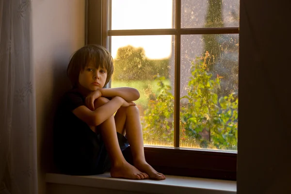 Szomorú gyermek, fiú, ül egy ablak pajzs — Stock Fotó