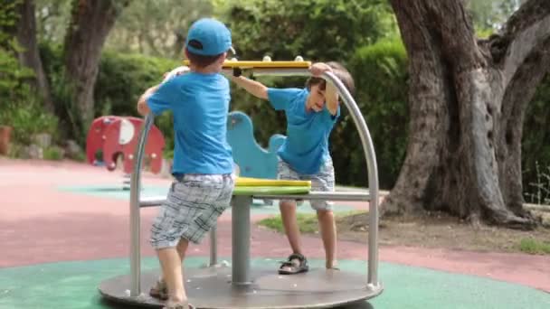 Zwei süße Kinder, die auf dem Spielplatz spielen, auf einem Kreisverkehr schaukeln, wirbeln — Stockvideo