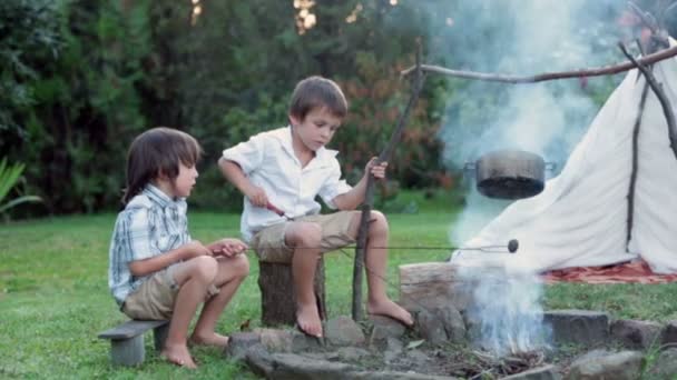 Två söta barn, pojke bröder, camping utanför sommartid på solnedgången, äta potatis — Stockvideo