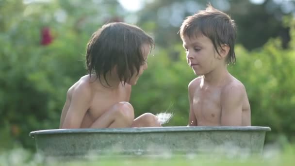 Dos niños, hermanos varones, bañándose al aire libre, haciendo pompas de jabón, en verano — Vídeo de stock